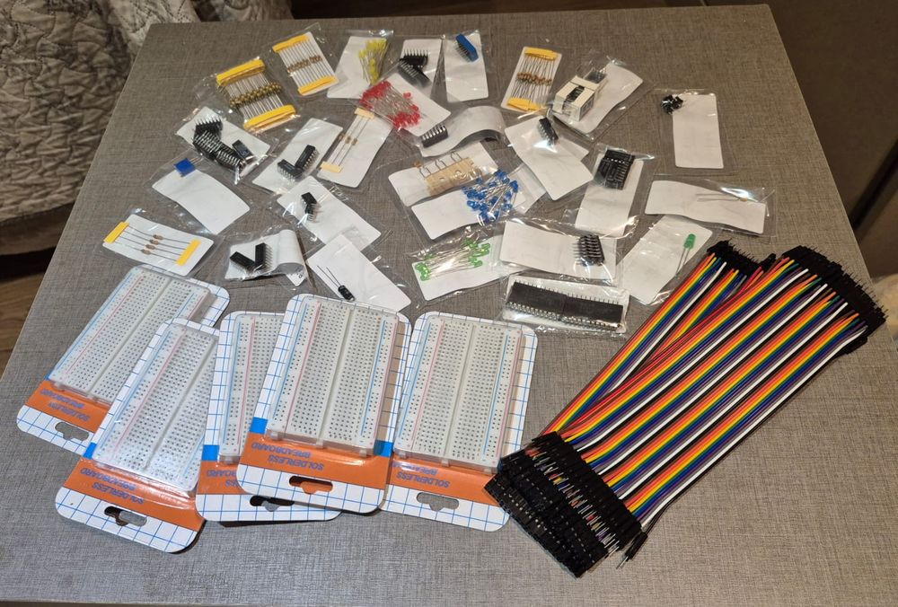 Componentes comprados para a montagem física: protoboards, resistores, LEDs, chips e jumpers, ainda embalados sobre a mesa